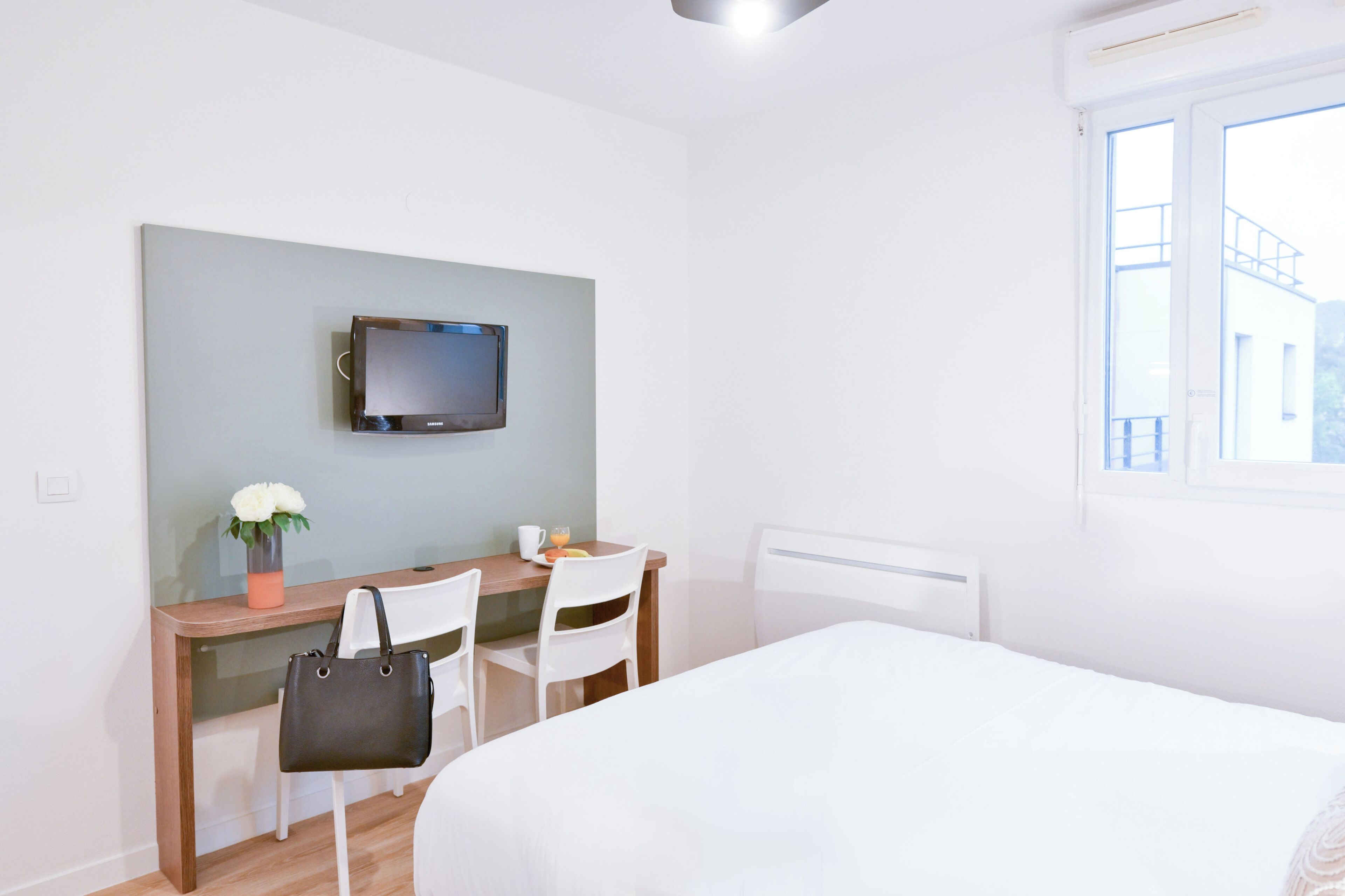 A hotel room with a bed, a desk with a chair, a television, and a window.