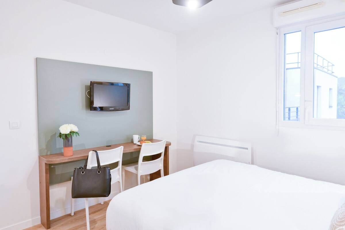 A hotel room with a bed, a desk with a chair, a television, and a window.