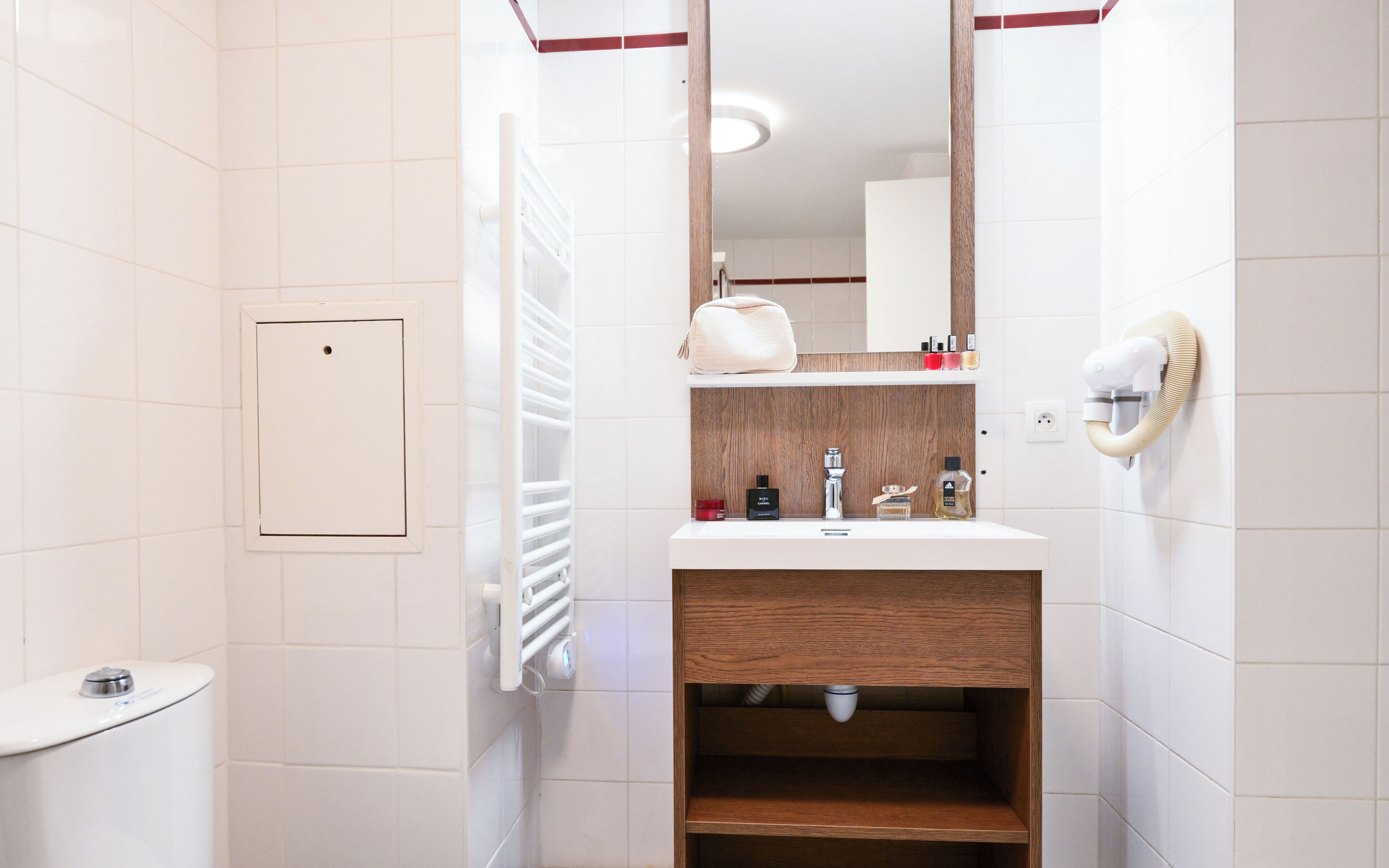 Un baño moderno con inodoro blanco, lavamanos con tocador de madera, espejo y barra para toallas.