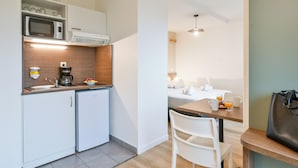 A compact kitchenette with a microwave, coffee maker, and small refrigerator. There is a dining area with a table, chairs, and a bag on a bench.
