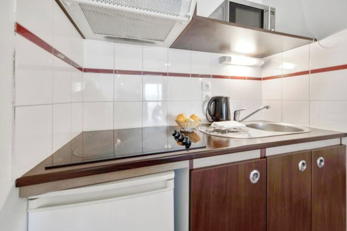 A modern kitchen with white tiles, a stainless steel sink, and wooden cabinets.