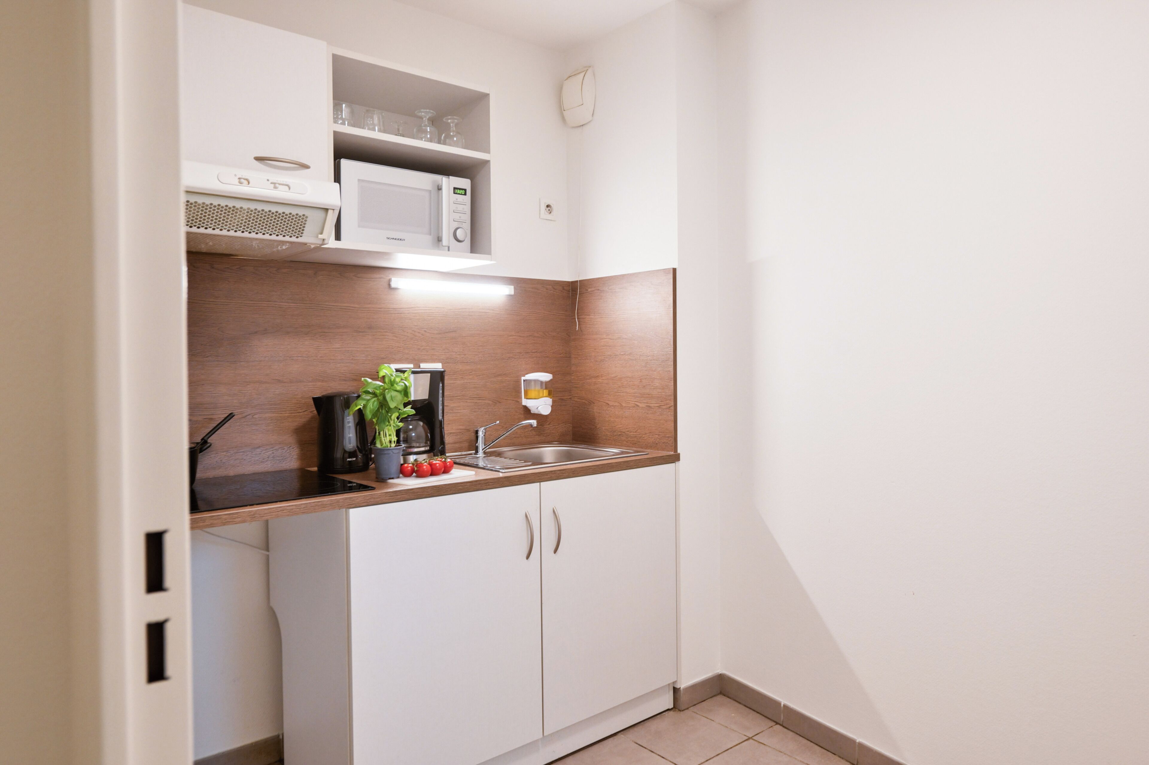 Una cucina compatta con mobili bianchi, un forno a microonde, una macchina da caffè e un lavandino.