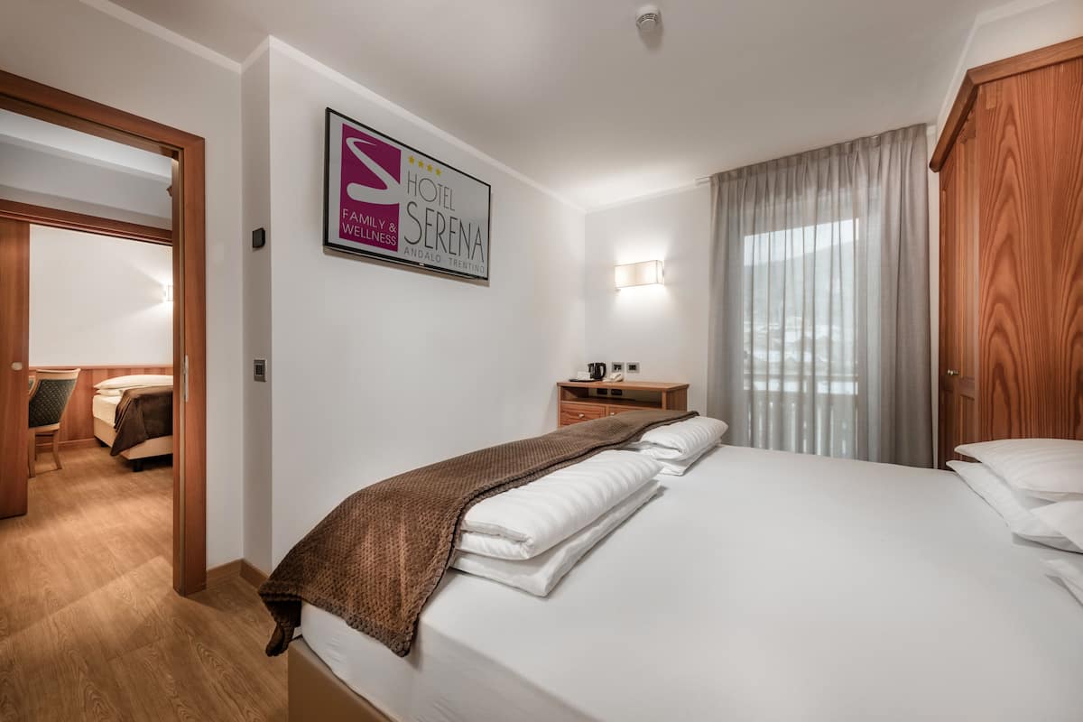 Une chambre d’hôtel comprenant un lit, une table de chevet, une lampe, une fenêtre avec des rideaux et une porte donnant sur une autre pièce.