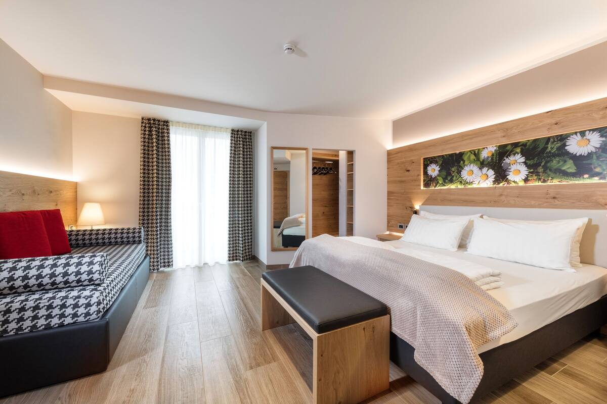 Une chambre moderne avec un grand lit, un banc, un canapé et une armoire.