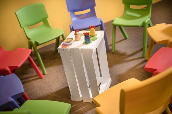 Una habitación con sillas de plástico de colores dispuestas alrededor de una mesa blanca con juguetes.