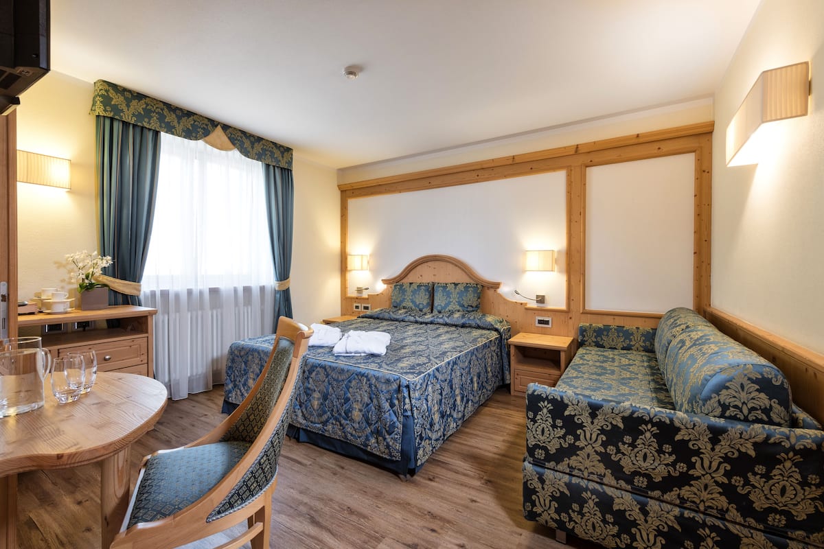 Une chambre d’hôtel avec un lit en bois, un canapé, une chaise, une petite table avec des verres et une lampe.