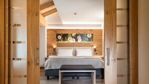 Ein modernes Schlafzimmer mit einem Holzkopfteil, einem großen Bett mit weißer Bettwäsche, einer Bank am Fußende des Bettes und einem an der Wand hängenden Blumenbild.