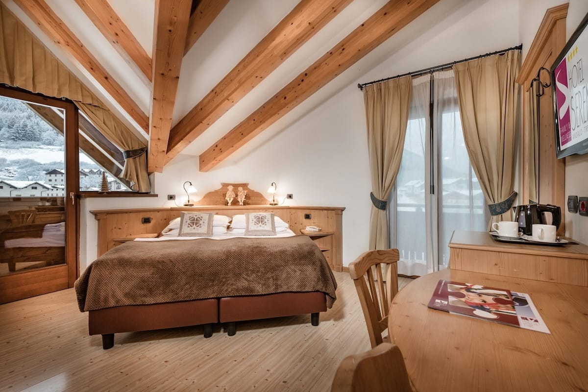 Une chambre confortable avec un lit en bois, un bureau doté d’une machine à café et une vue sur les maisons enneigées par la fenêtre.