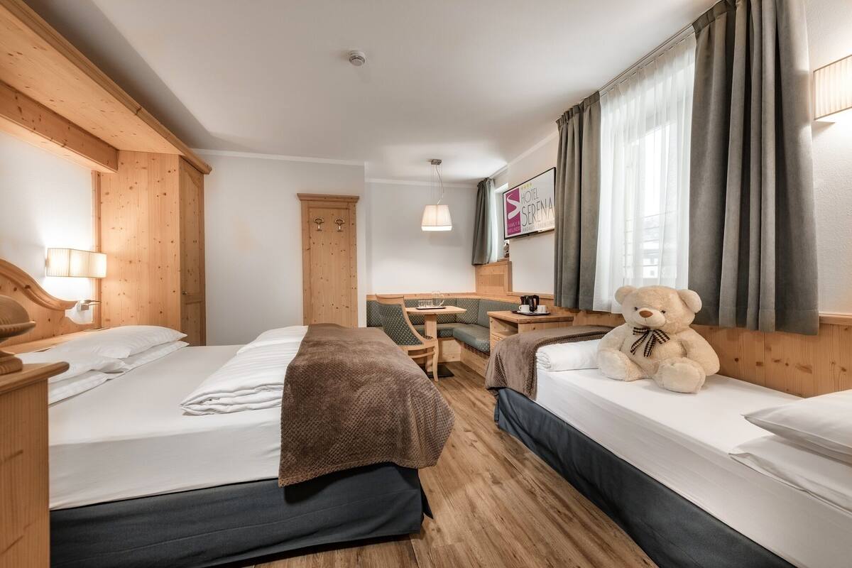 Une chambre d’hôtel avec deux lits, une petite table, une chaise et un ours en peluche.