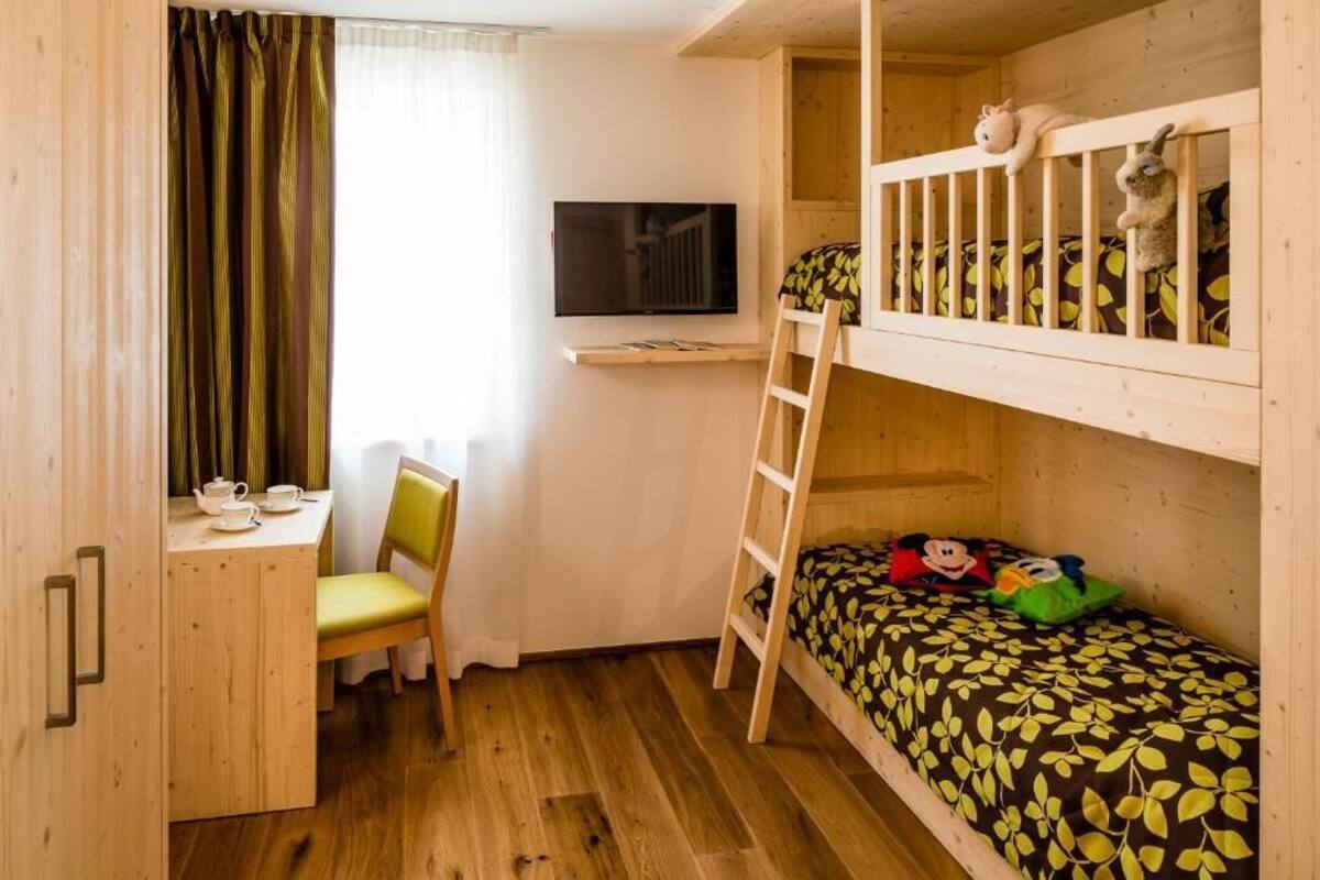 Une chambre confortable avec un lit superposé, un bureau avec une chaise, une télévision et une fenêtre avec des rideaux.