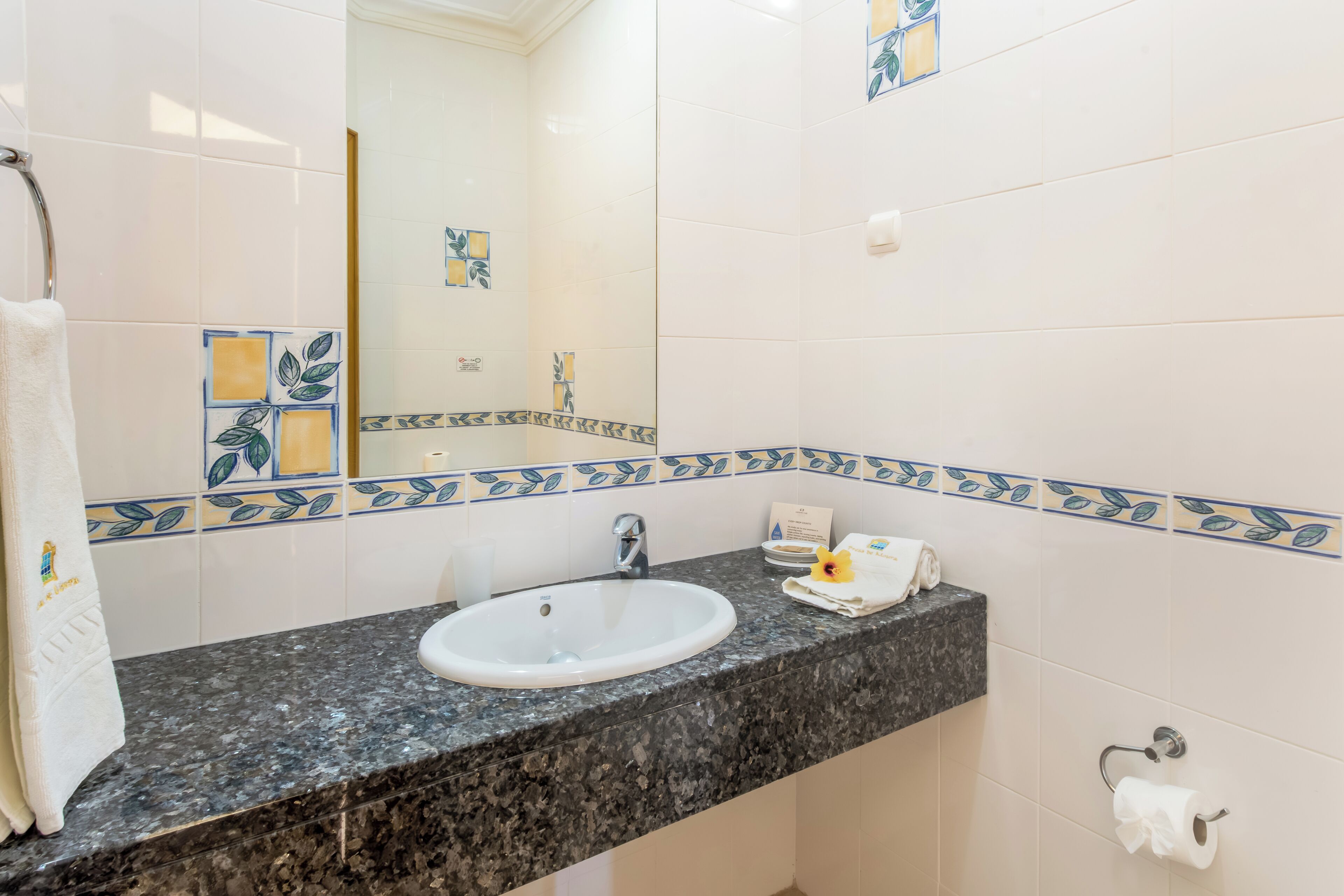 Casa de banho com lavatório branco, bancada de granito escuro e azulejos decorativos.