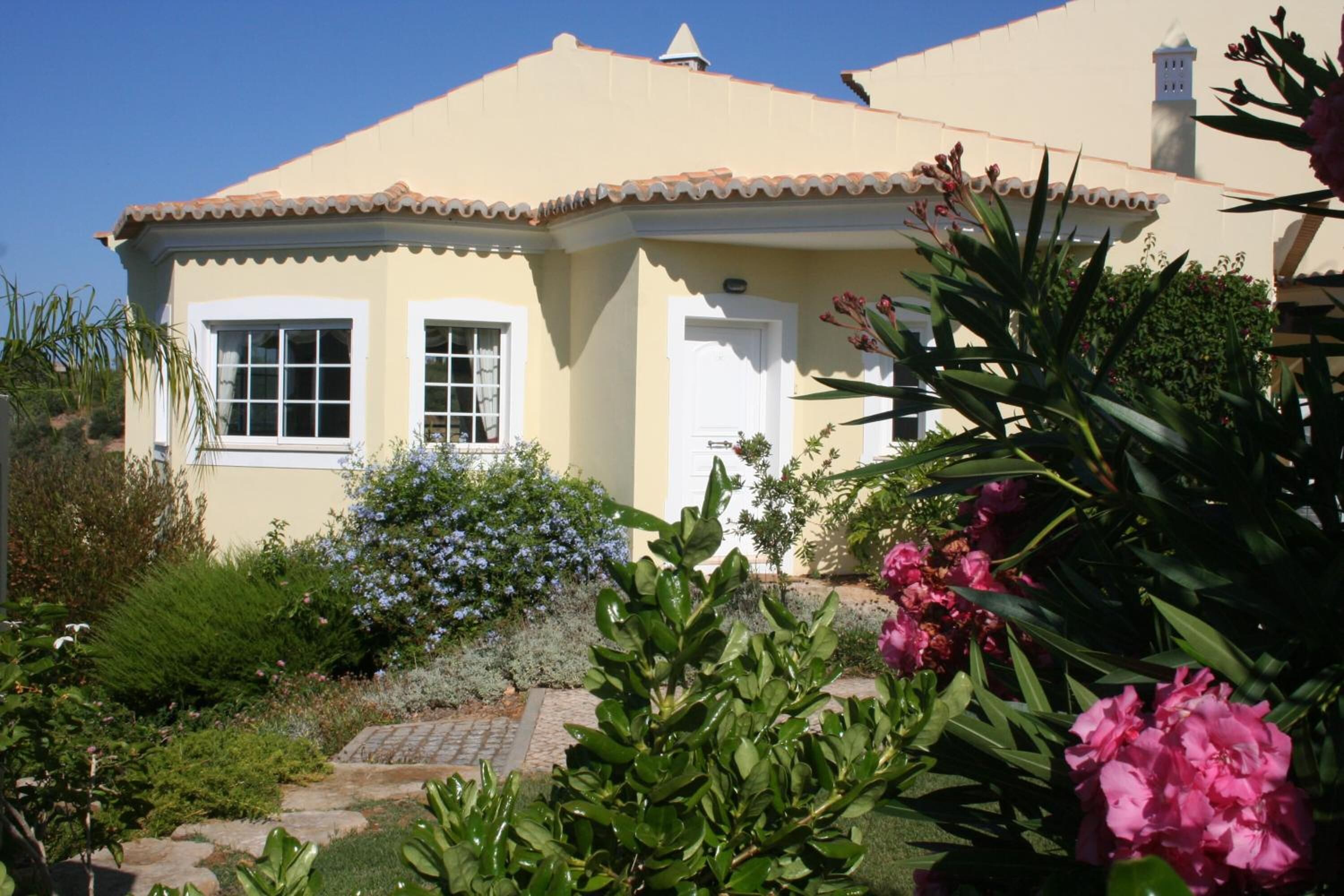 A house with a tiled roof, a front door, and a small garden with various plants and flowers.