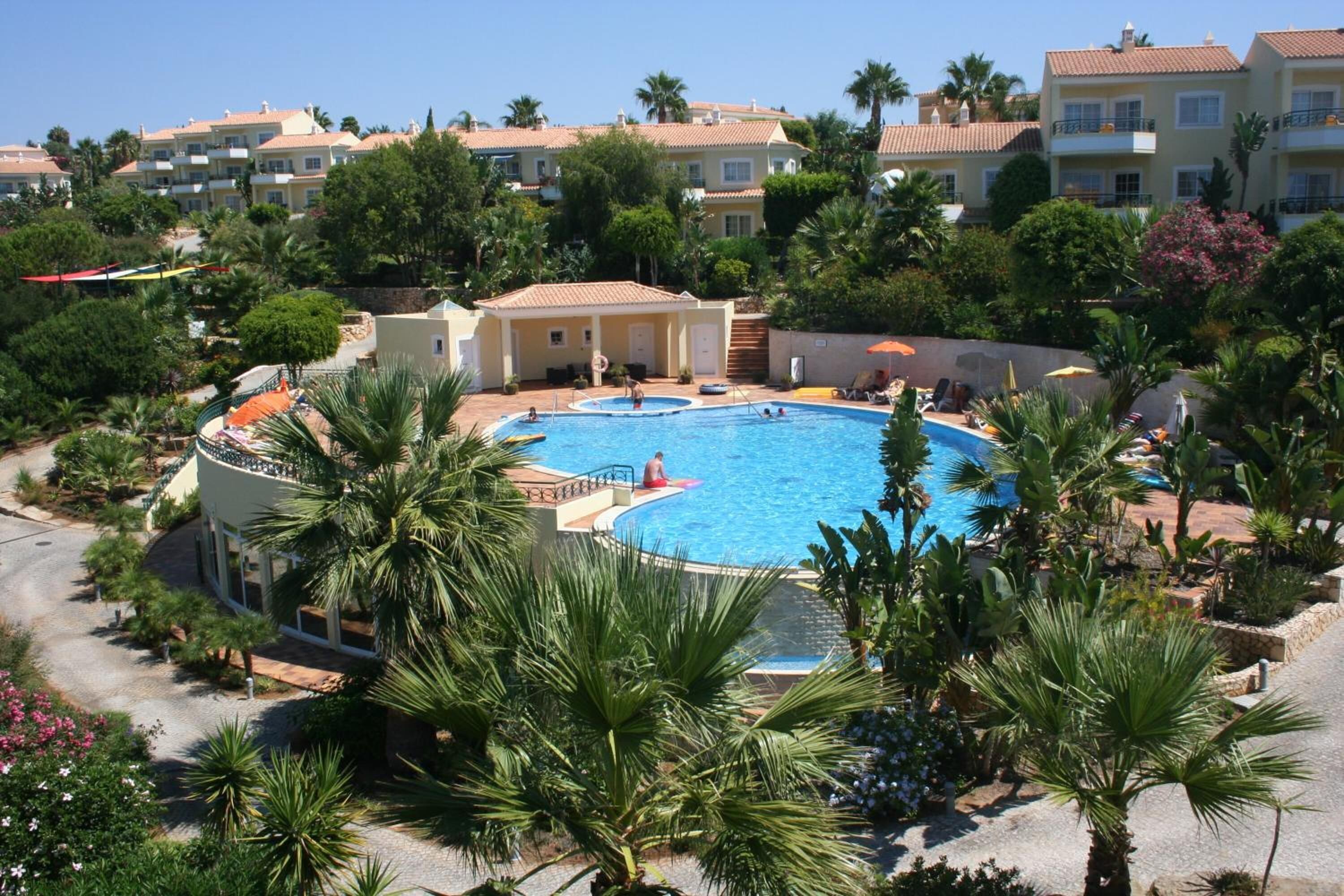 A resort with a central swimming pool surrounded by palm trees and lounge chairs.