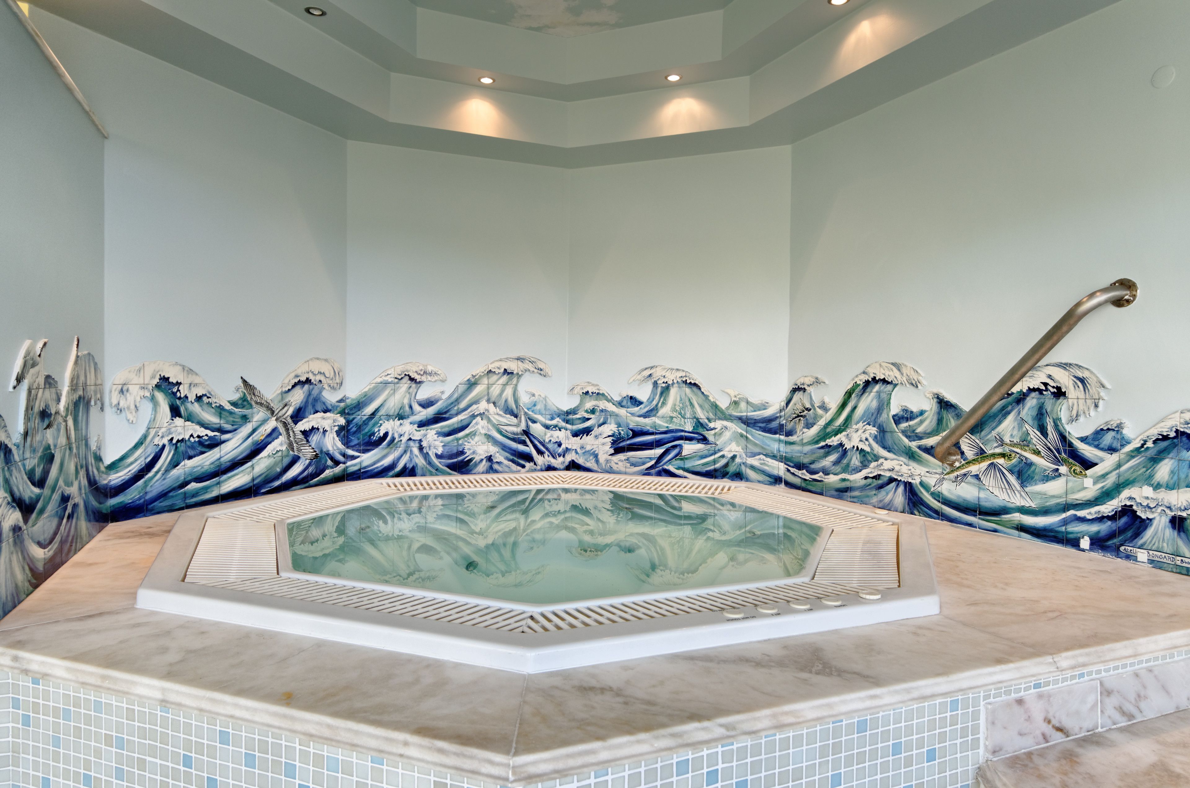 A spa area with a large hot tub surrounded by a wave-themed mural.