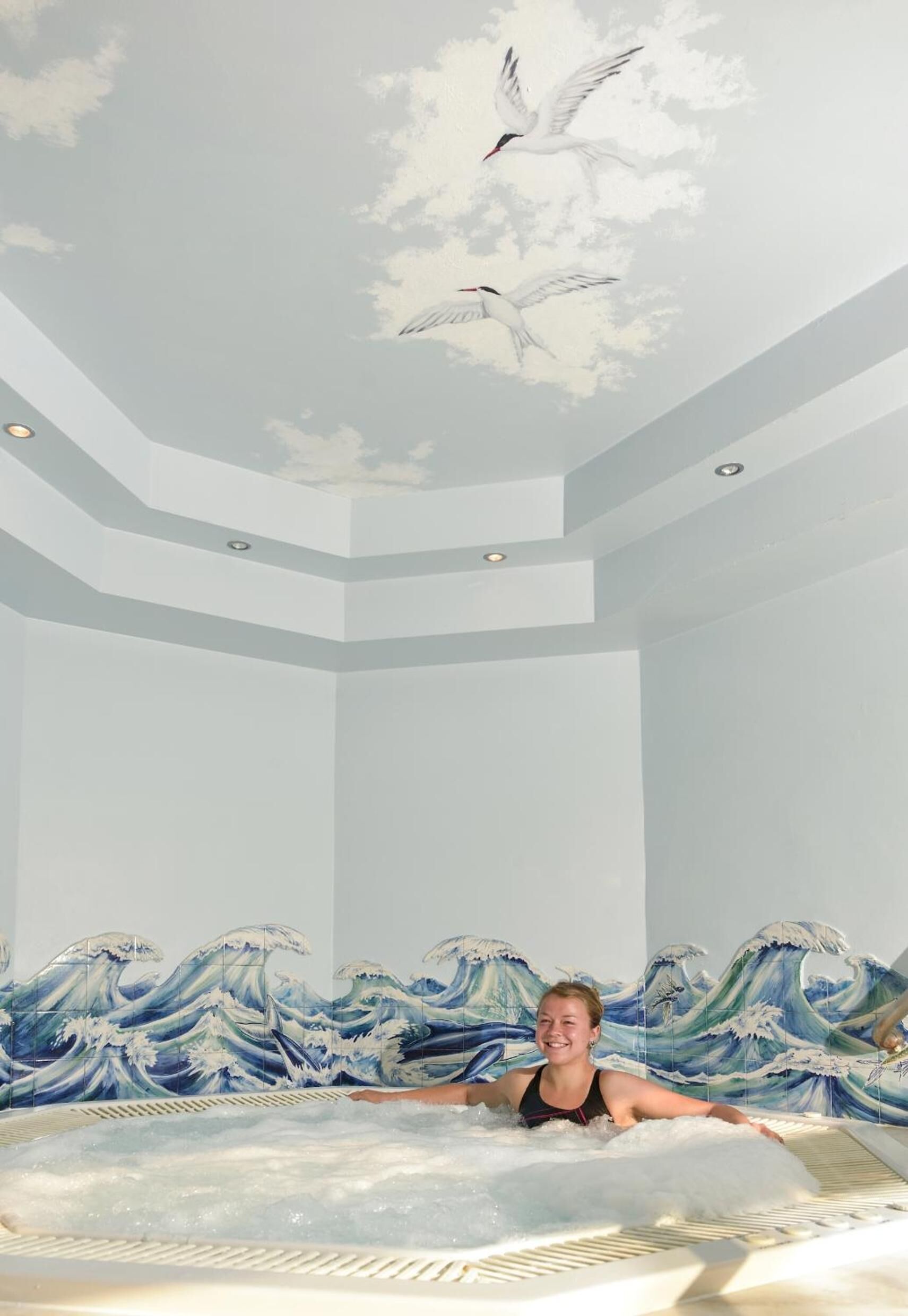 A person in a bathtub with a wave pattern on the wall behind them.
