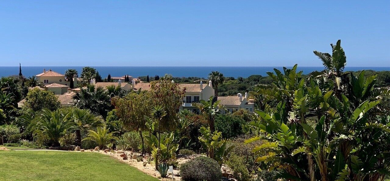 A coastal residential area with houses, lush greenery, and a clear view of the sea.
