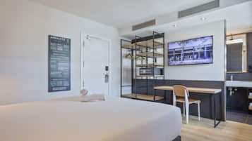 Ett modernt hotellrum med en stor säng, ett skrivbord och en tv som är monterad på väggen.