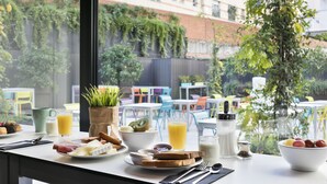 A breakfast table with various food items and drinks, a potted plant, and a view of an outdoor area with tables and chairs. - Hotel Andante Drassanes (Barcelona)