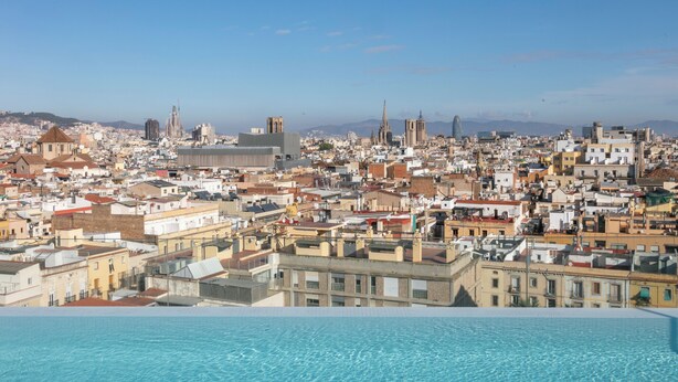 A cityscape with a pool in the foreground, buildings, and a distant cathedral. - Hotel Andante Drassanes (Barcelona)