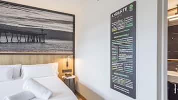 Habitació d'hotel amb un llit, una tauleta de nit, un cartell fixat a la paret que explica les iniciatives de sostenibilitat de l'hotel i una fotografia gran amb un moll.