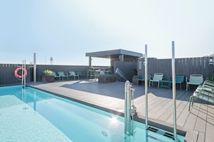 Una piscina en la azotea con un flotador salvavidas, sillas de descanso y un área de estar techada.