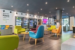A modern lobby with colorful chairs, recycling bins, vending machines, and a digital display.