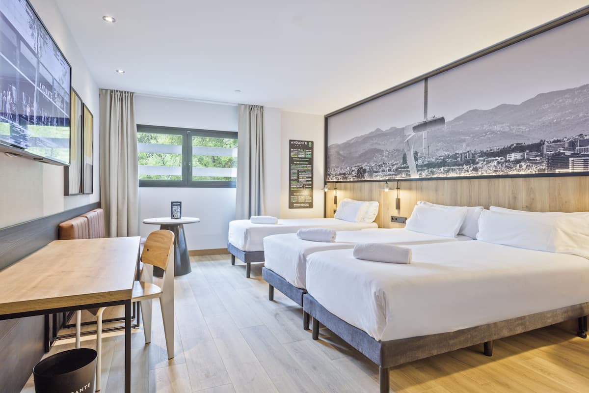 A hotel room with three beds, a dining table, and a view of a cityscape through the window.