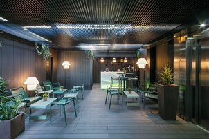 An outdoor seating area with green chairs and tables, a bar counter, and a ceiling with linear patterns.