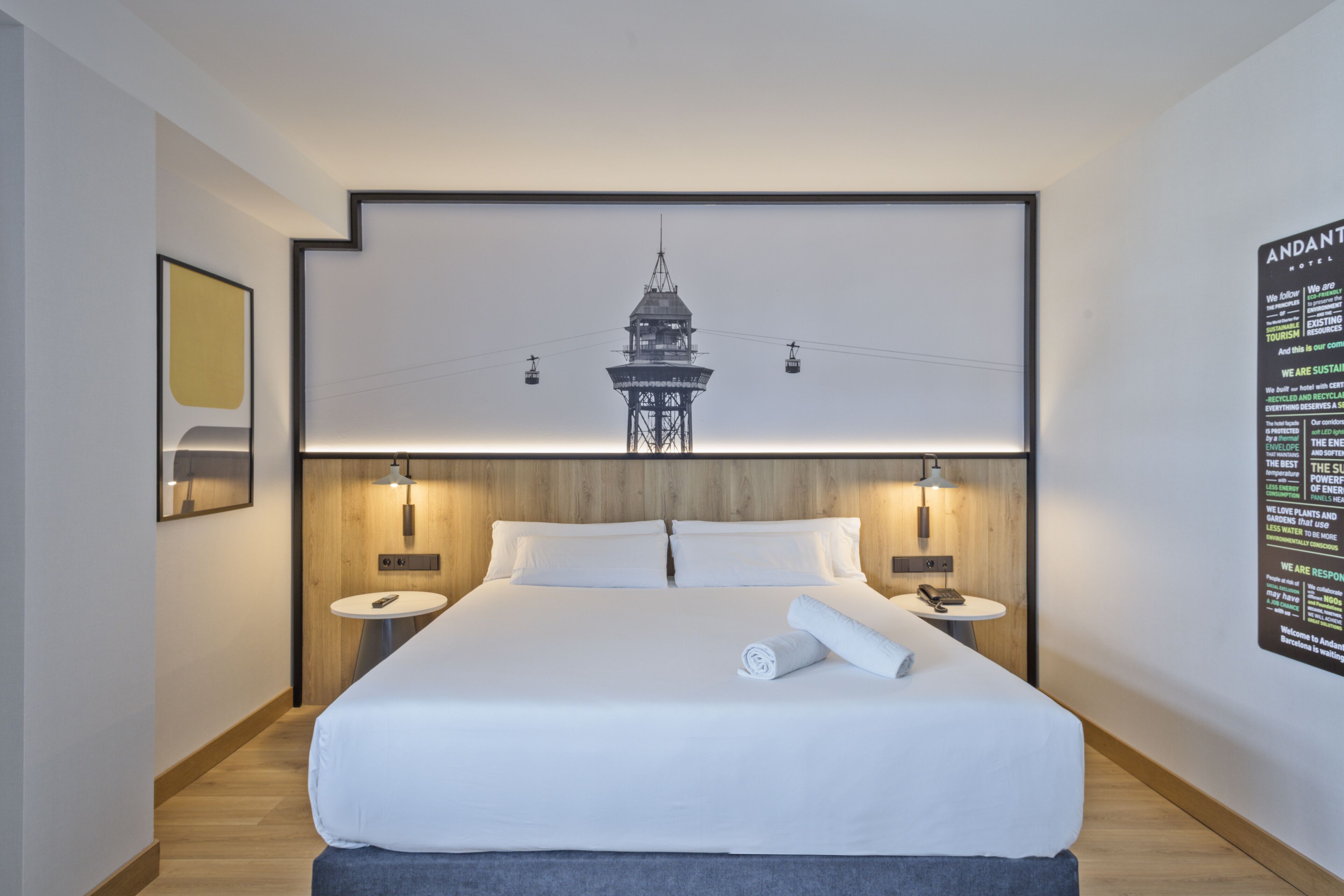 Una habitación de hotel moderna con una cama grande, dos mesitas de noche, un televisor de pared y un cartel en la pared.