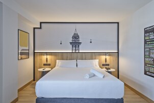 A modern hotel room with a large bed, two bedside tables, a wall-mounted TV, and a poster on the wall.