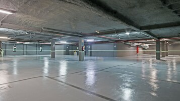 Um estacionamento subterrâneo com pilares de concreto, faixas demarcadas em verde e branco e equipamentos de emergência.