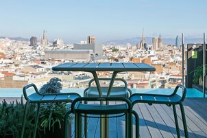 A rooftop terrace with a table and chairs, overlooking a cityscape with various buildings.