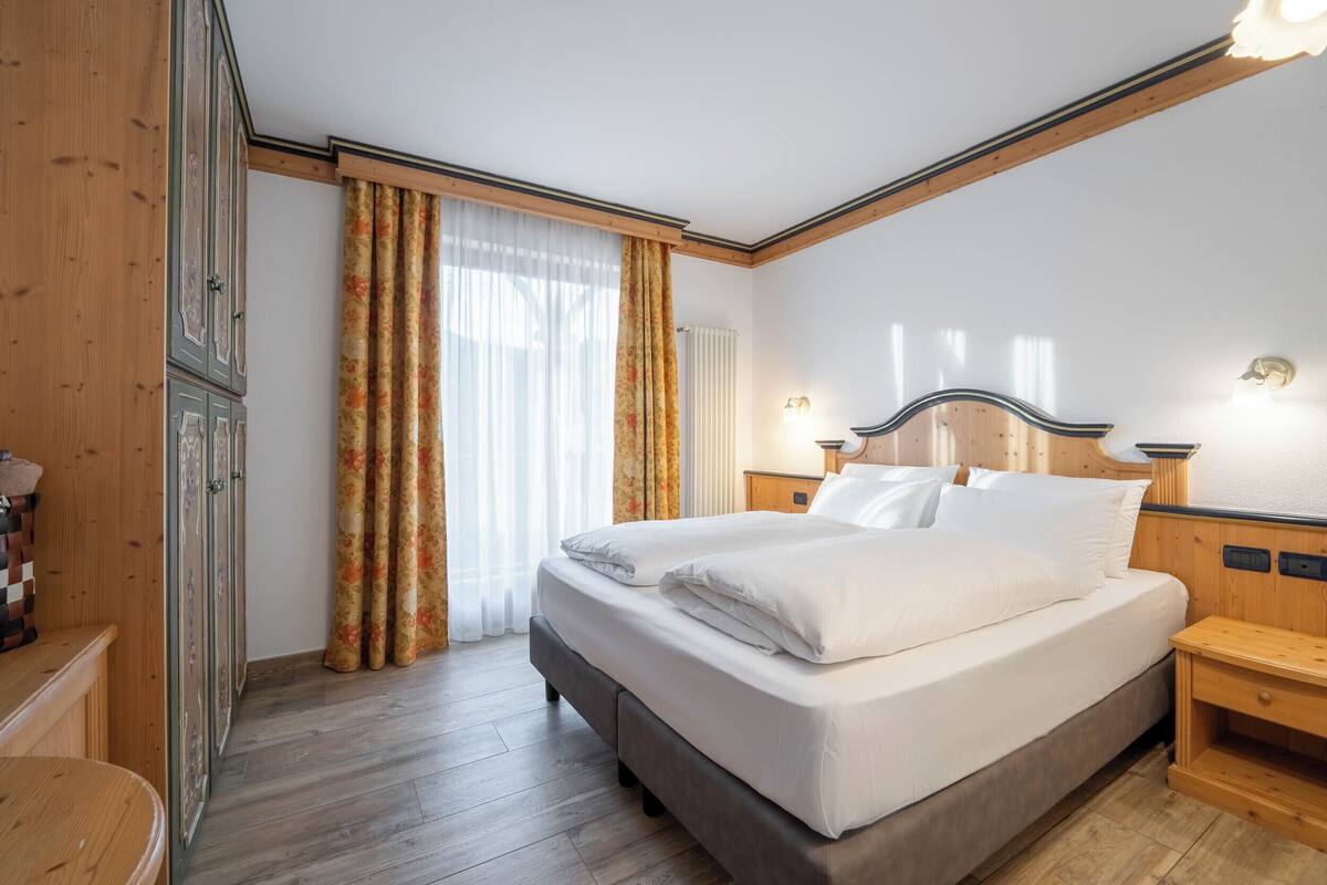 A bedroom with a large bed, wooden wardrobe, and a nightstand.