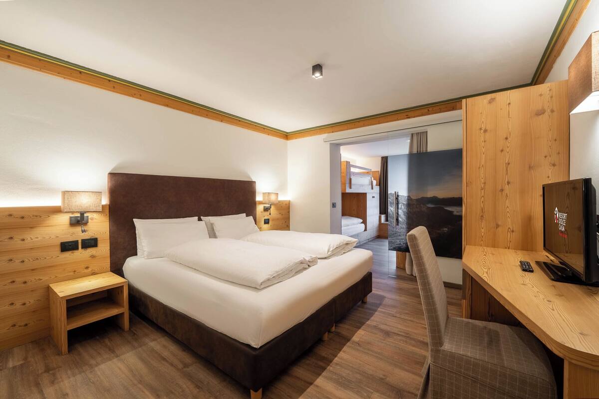 A hotel room with a large bed, bedside tables, a desk with a chair, and a television.
