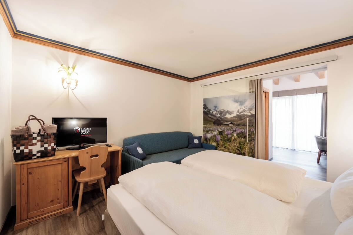 A hotel room with a bed, a desk with a television, a chair, and a sofa.