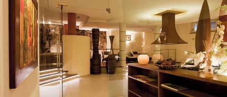 A modern hotel lobby with a glass partition, a staircase, a reception desk, and a decorative vase with flowers.