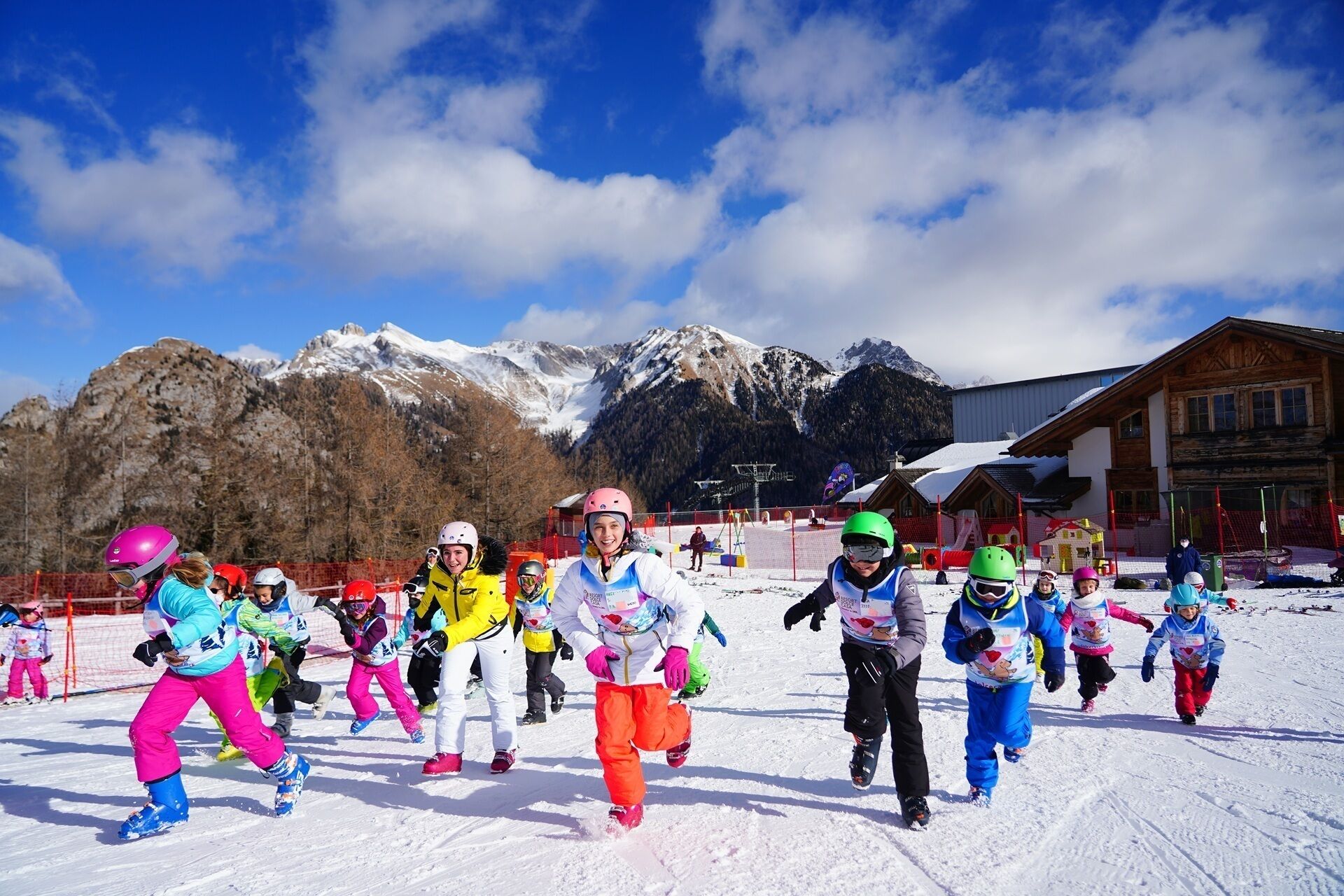 Un grupo de niños esquiando en una pendiente nevada con montañas al fondo.