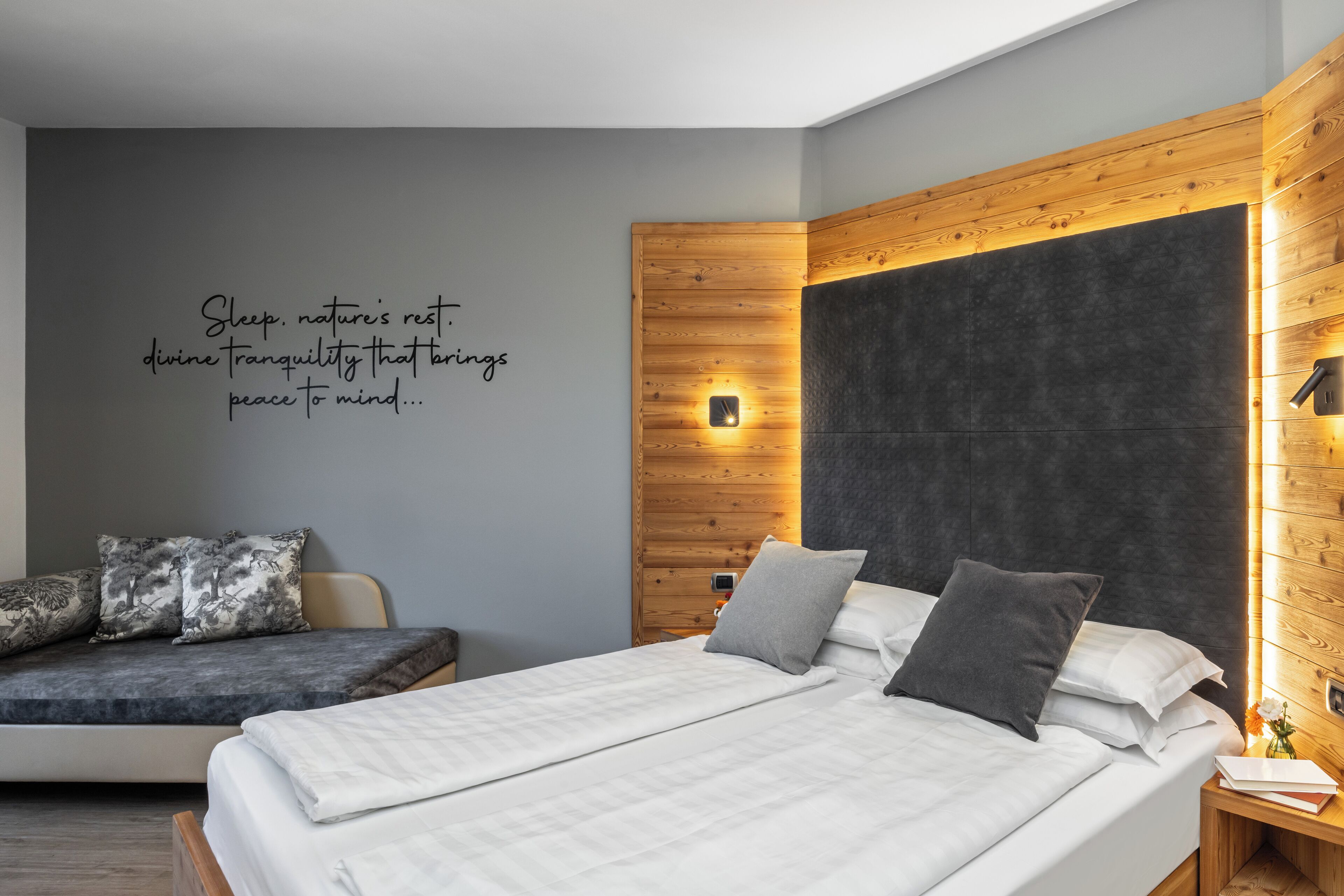 A modern bedroom with a bed, a bench, and a wall with a quote.
