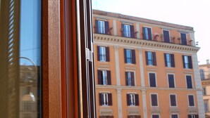 A window with a wooden frame and a view of a multi-story building with balconies and windows. - Hotel Trastevere (Rome)