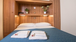 A hotel room with a bed, two white towels, a blue bedspread, a wooden shelf with plants, and a phone on the shelf. - Hotel Trastevere (Rome)