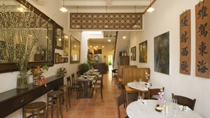 A restaurant with wooden tables and chairs, a long counter with a vase of flowers, and artwork on the walls. - 23 LoveLane Penang (George Town)