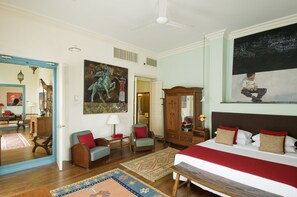 A spacious bedroom with a large bed, a wooden wardrobe, a sitting area with a chair and a small table, and a large mirror.