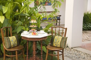 A round wooden table with a white tablecloth, two wooden chairs with patterned cushions, and a tiered dessert stand.