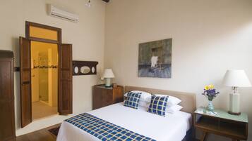 A bedroom with a bed, a nightstand, a lamp, a painting, and a door to a bathroom.