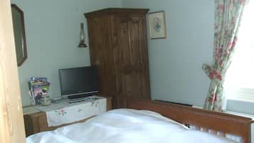 Un dormitorio con cama, armario de madera, televisor sobre una mesa y ventana con cortinas estampadas.