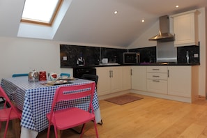 Cocina compacta con zona de comedor, que incluye un mantel a cuadros, sillas rosas y un tragaluz.