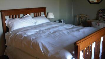 Een net opgemaakt bed met een houten hoofdbord en witte beddengoed in een kamer met een klein tafeltje en een lamp.