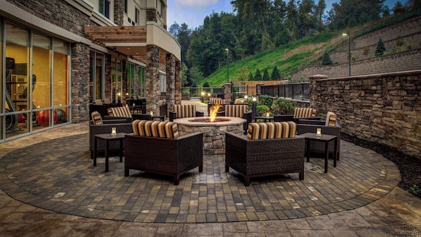 A patio area with wicker furniture and a central fire pit, surrounded by stone walls and a view of a hillside. - Courtyard Boone (Boone)