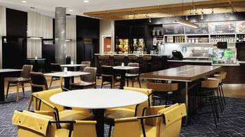 A modern restaurant with round tables and yellow chairs, a bar area with menu boards, and a coffee machine.