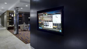 A modern lobby with a digital display showing news and weather, a reception desk, and a patterned carpet. - Courtyard Boone (Boone)
